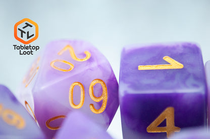 A close up of the Purple Jade 7 piece dice set from Tabletop Loot with swirled purple and white resin and gold numbering.
