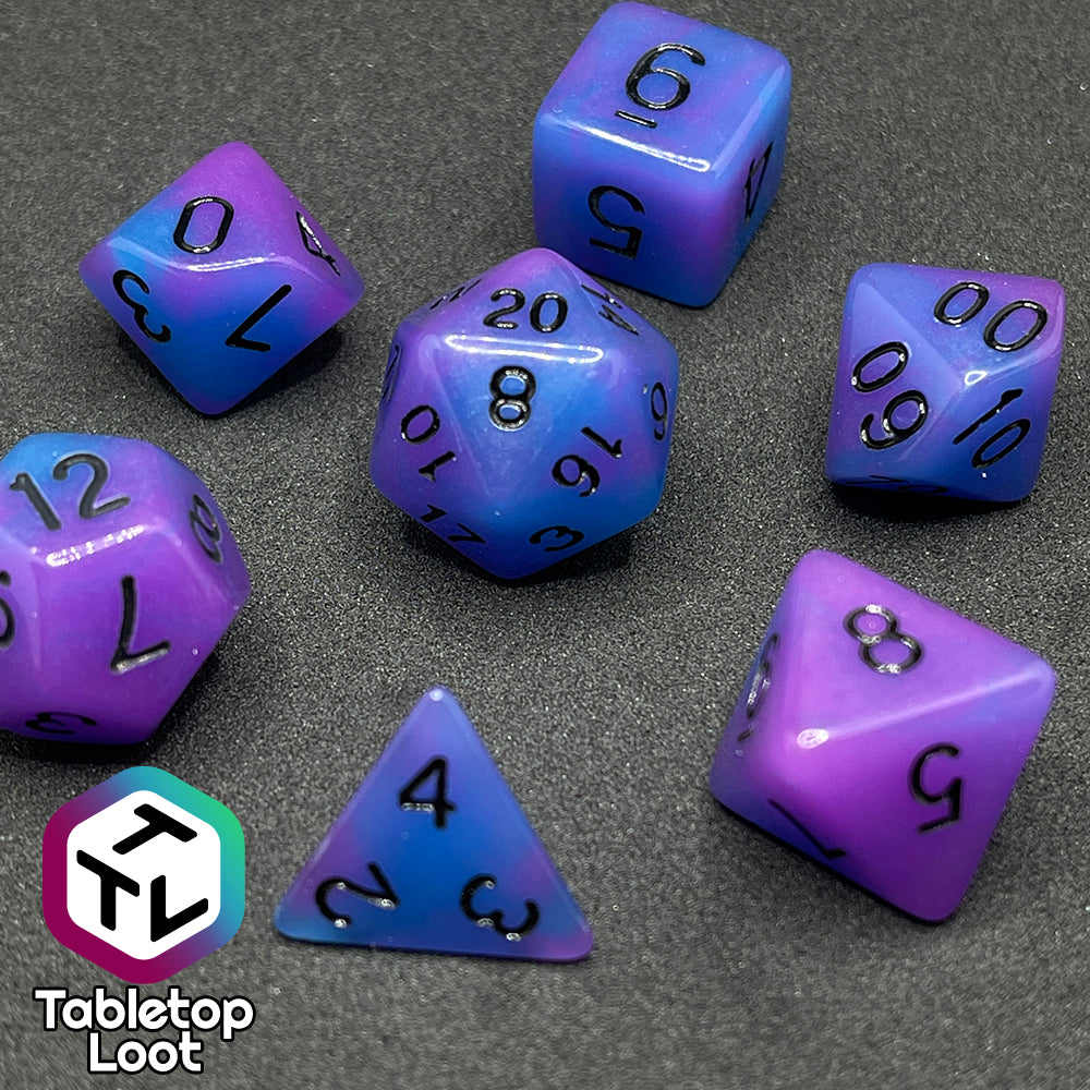 The Quantum 7 piece dice set from Tabletop Loot with swirls of blue and purple glow pigment and black numbering, shown in light.
