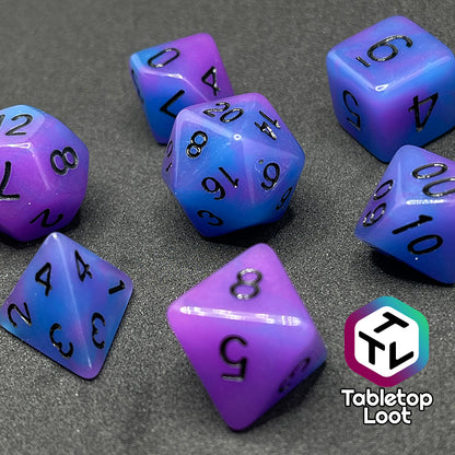 A close up of the Quantum 7 piece dice set from Tabletop Loot with swirls of blue and purple glow pigment and black numbering, shown in light.