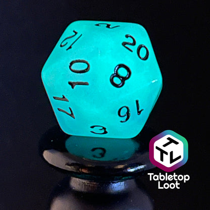 A close up of the D20 from the Quantum 7 piece dice set from Tabletop Loot with swirls of blue and purple glow pigment and black numbering, shown glowing.