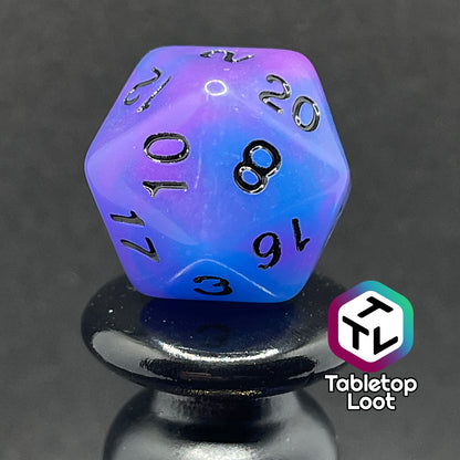 A close up of the D20 from the Quantum 7 piece dice set from Tabletop Loot with swirls of blue and purple glow pigment and black numbering, shown in light.