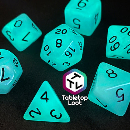 A close up of the Quantum 7 piece dice set from Tabletop Loot with swirls of blue and purple glow pigment and black numbering, shown glowing.