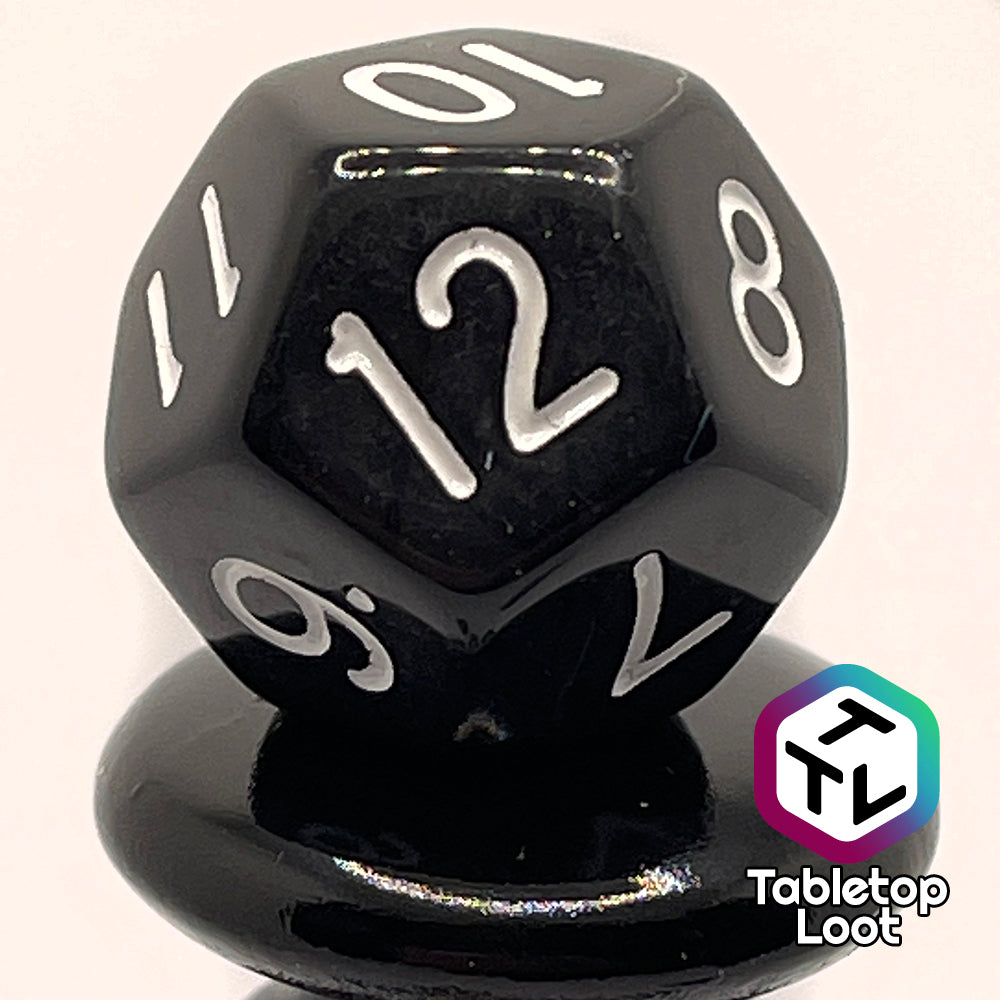 A close up of the D12 from the Ravenous Void 7 piece dice set; solid black with white numbering.