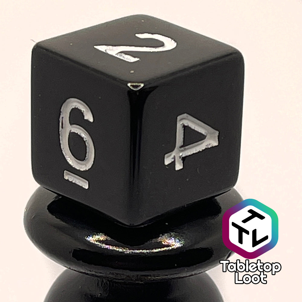 A close up of the D6 from the Ravenous Void 7 piece dice set; solid black with white numbering.