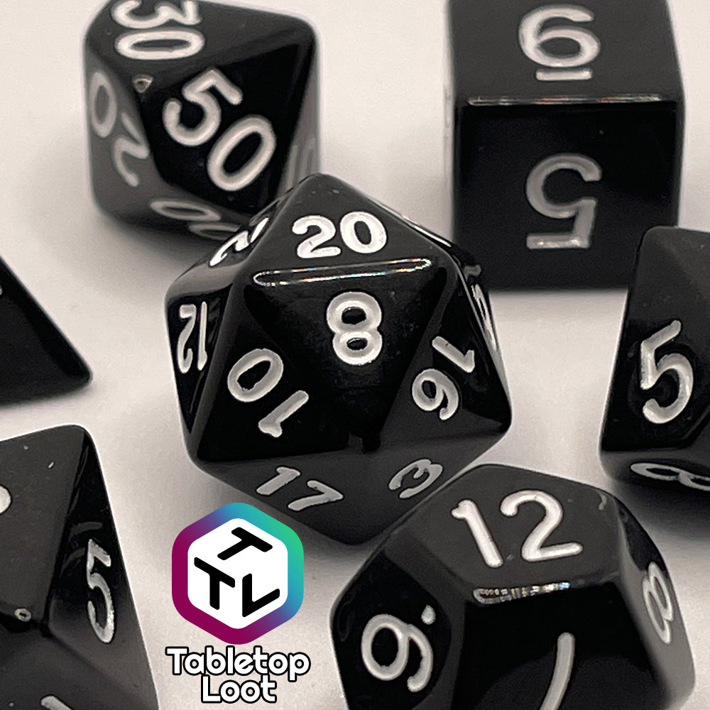 A close up of the Ravenous Void 7 piece dice set; solid black with white numbering.