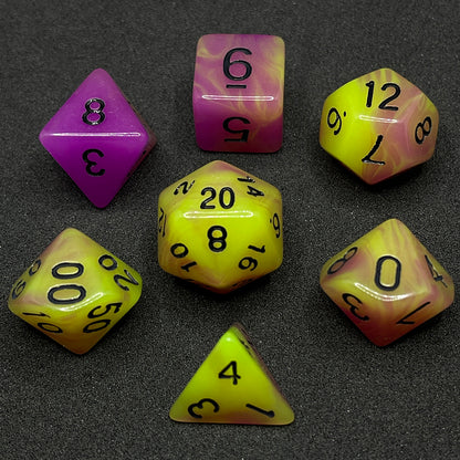 The Retro 80s glow in the dark 7 piece dice set from Tabletop Loot with swirls of pink and yellow glow pigment and black numbering, shown in light.