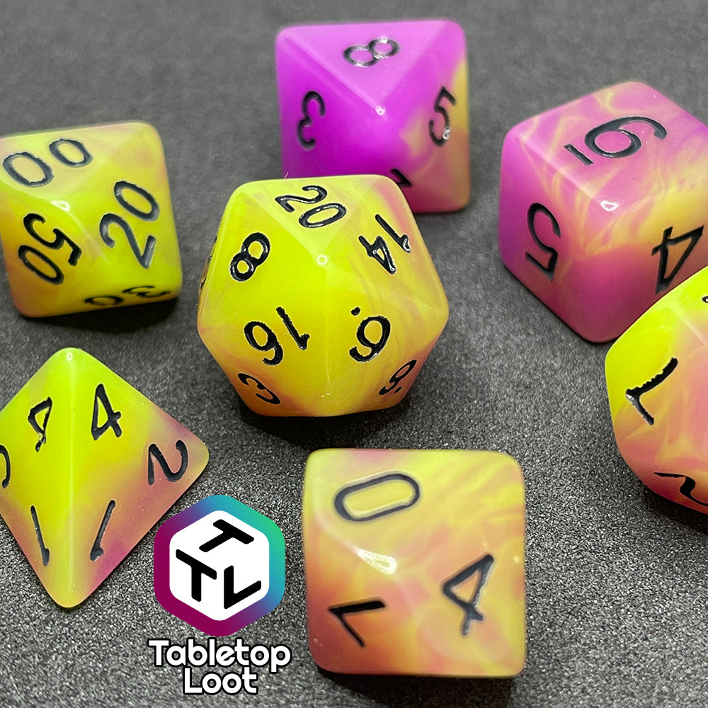 A close up of the Retro 80s glow in the dark 7 piece dice set from Tabletop Loot with swirls of pink and yellow glow pigment and black numbering, shown in light.