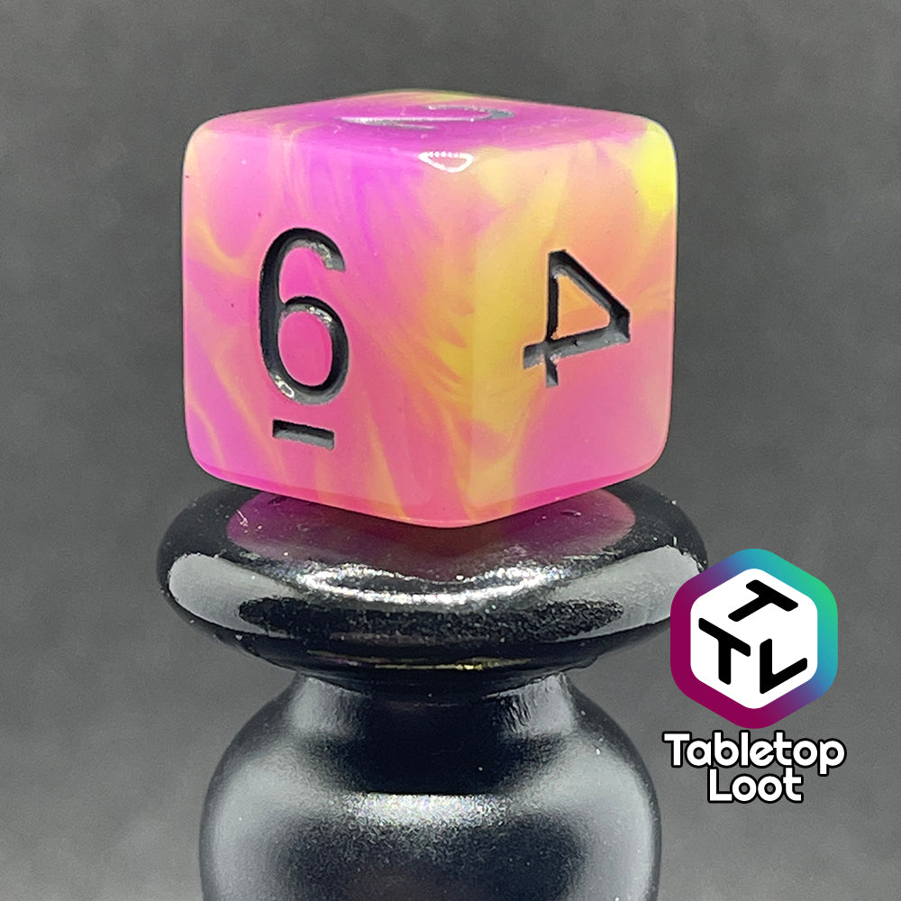 A close up of the D6 from the Retro 80s glow in the dark 7 piece dice set from Tabletop Loot with swirls of pink and yellow glow pigment and black numbering, shown in light.