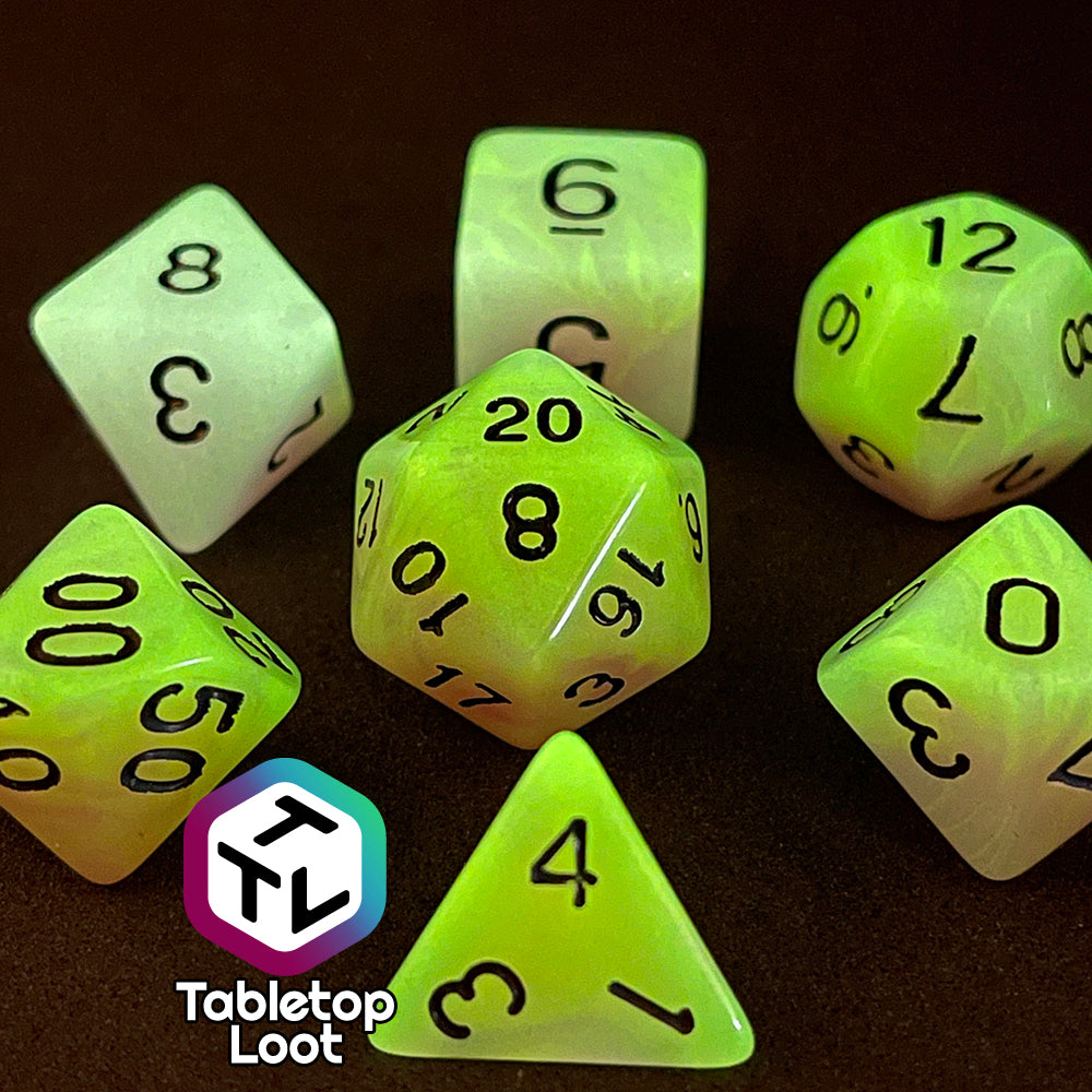 A close up of the Retro 80s glow in the dark 7 piece dice set from Tabletop Loot with swirls of pink and yellow glow pigment and black numbering, shown glowing.