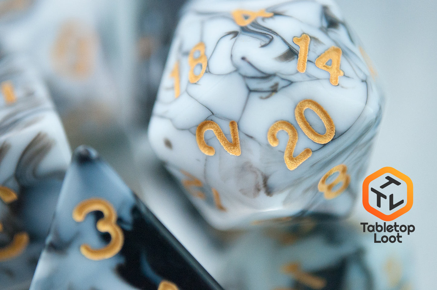 A close up of the D20 from the Rolling Thunder 7 piece dice set from Tabletop Loot with swirls of white, grey, and black resin and gold numbering.