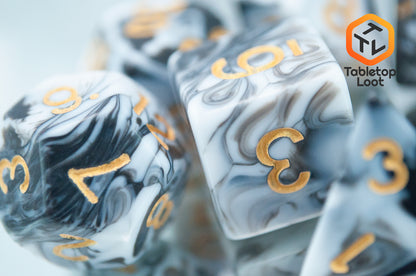 A close up of the D6 from the Rolling Thunder 7 piece dice set from Tabletop Loot with swirls of white, grey, and black resin and gold numbering.