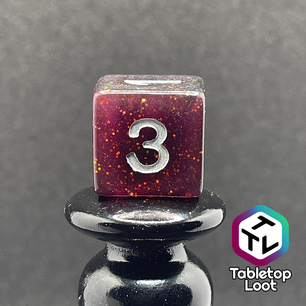 A close up of the D6 from the Rosavalda 7 piece dice set from Tabletop Loot, ultra dark purple dice with golden glitter and white numbering.