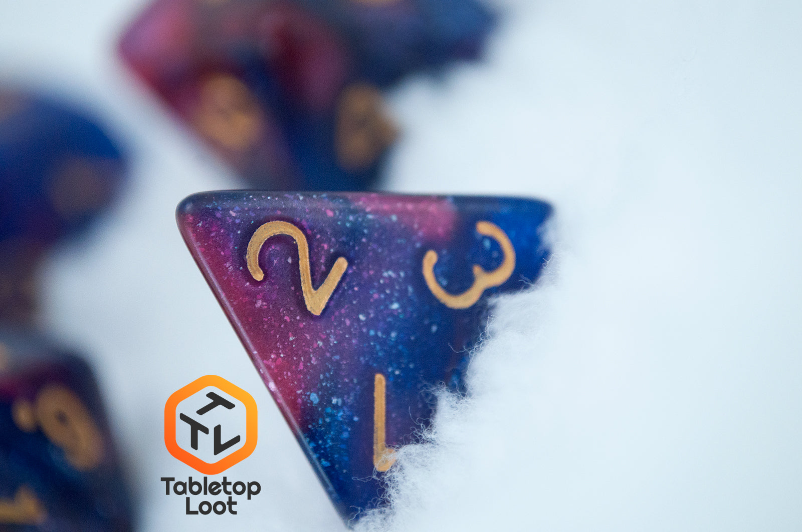 A close up of the D4 from the Rose Galaxy 7 piece dice set from Tabletop Loot with swirls of glittery pink, purple, and blue throughout with gold numbering.