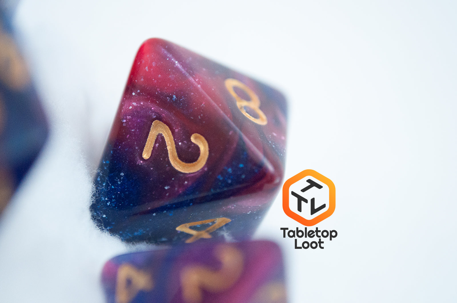 A close up of the D8 from the Rose Galaxy 7 piece dice set from Tabletop Loot with swirls of glittery pink, purple, and blue throughout with gold numbering.