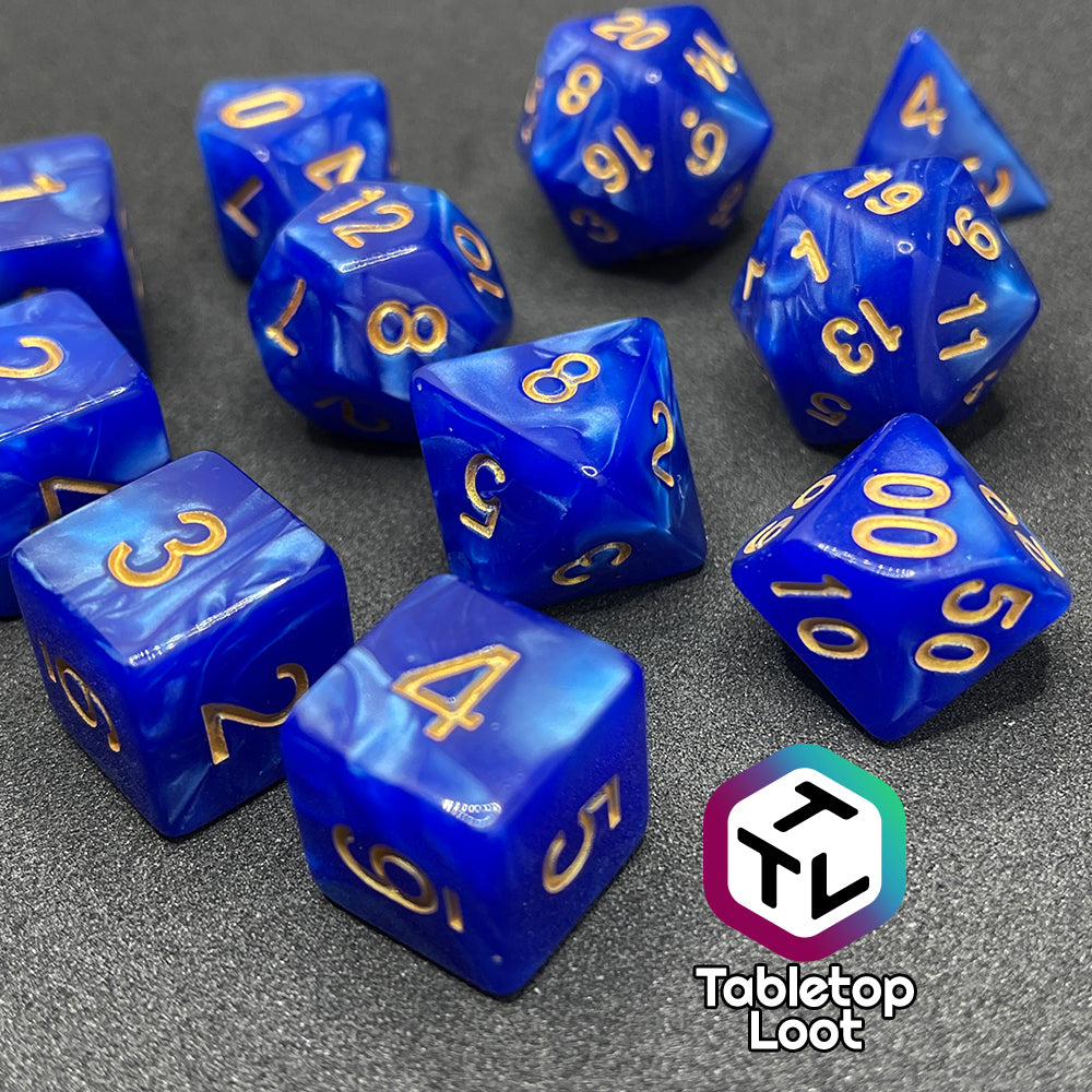 A close up of the Royal Sapphire 11 piece dice set from Tabletop Loot with swirls of pearlescent blue and gold numbering.