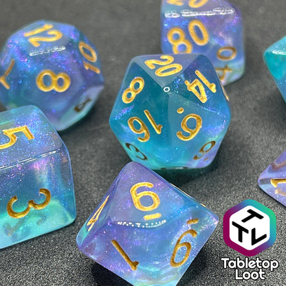 A close up of the Shape Water 7 piece dice set from Tabletop Loot with swirls of glittery purple and blue resin and gold numbering.