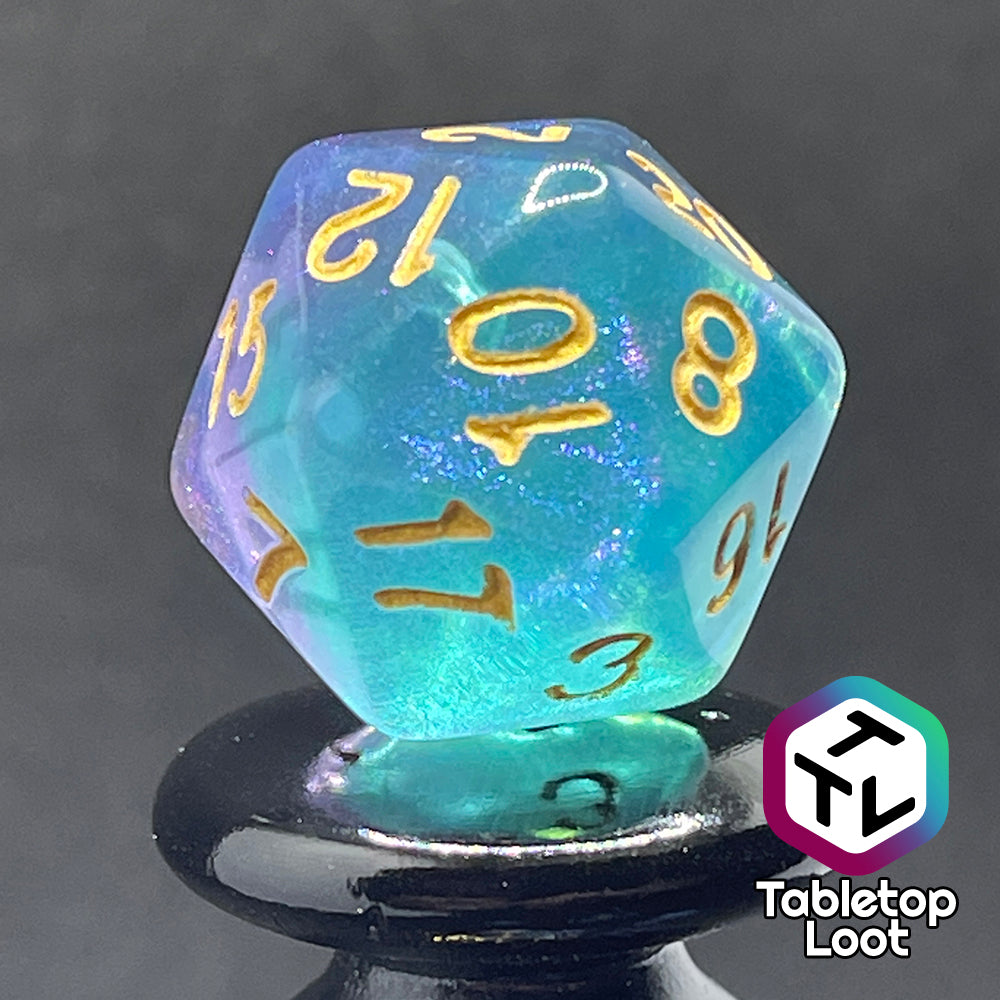 A close up of the D20 from the Shape Water 7 piece dice set from Tabletop Loot with swirls of glittery purple and blue resin and gold numbering.
