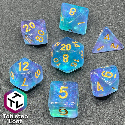 The Shape Water 7 piece dice set from Tabletop Loot with swirls of glittery purple and blue resin and gold numbering.