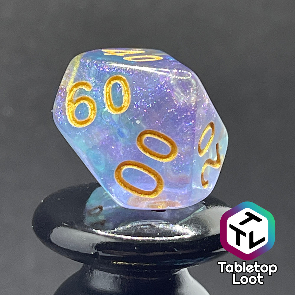 A close up of the percentile die from the Shape Water 7 piece dice set from Tabletop Loot with swirls of glittery purple and blue resin and gold numbering.