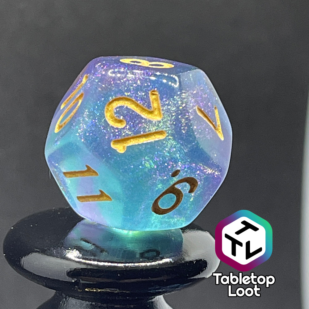 A close up of the D12 from the Shape Water 7 piece dice set from Tabletop Loot with swirls of glittery purple and blue resin and gold numbering.