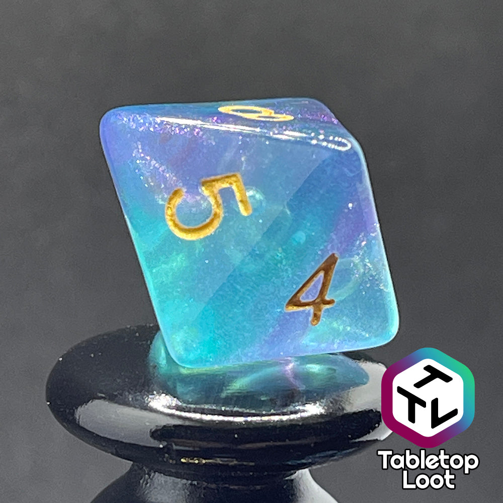A close up of the D8 from the Shape Water 7 piece dice set from Tabletop Loot with swirls of glittery purple and blue resin and gold numbering.