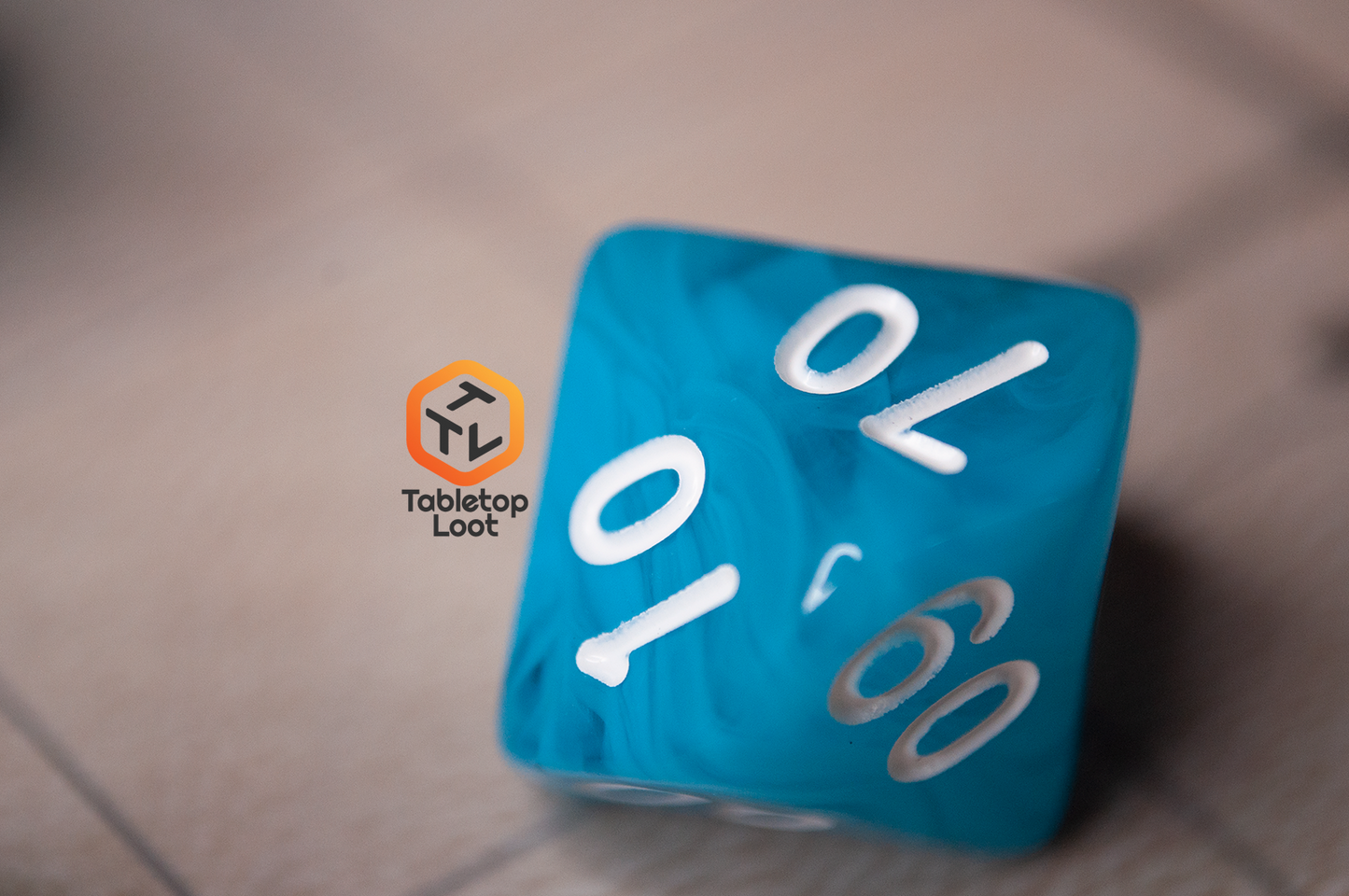 A close up of the percentile die from the Sky Blue 7 piece dice set from Tabletop Loot with blue and white swirls in clear resin and white numbering.