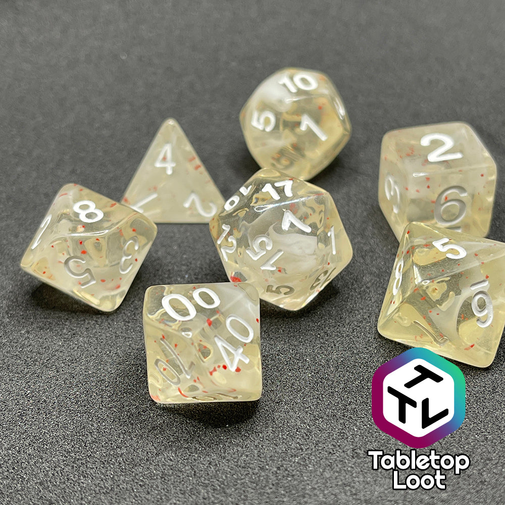 A close up of the Spore Cloud 7 piece dice set from Tabletop Loot with swirls of white and speckles of red suspended in clear resin and white numbering.