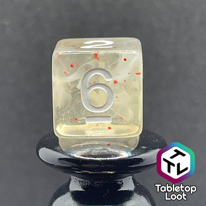 A close up of the D6 from the Spore Cloud 7 piece dice set from Tabletop Loot with swirls of white and speckles of red suspended in clear resin and white numbering.