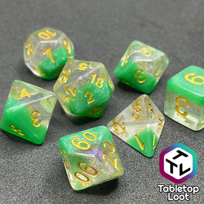A close up of the Spring Dew 7 piece dice set from Tabletop Loot with a layer of shimmery light green under shimmery clear resin and gold numbering.