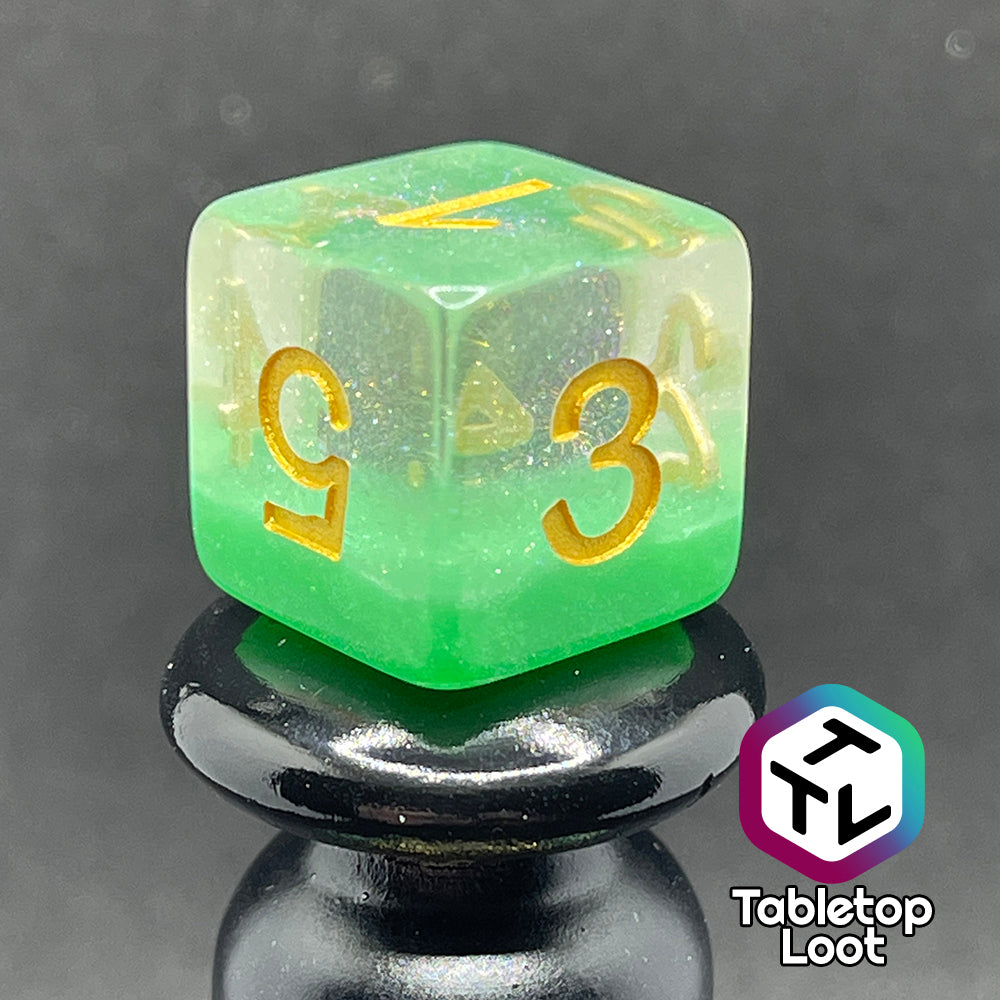 A close up of the D6 from the Spring Dew 7 piece dice set from Tabletop Loot with a layer of shimmery light green under shimmery clear resin and gold numbering.