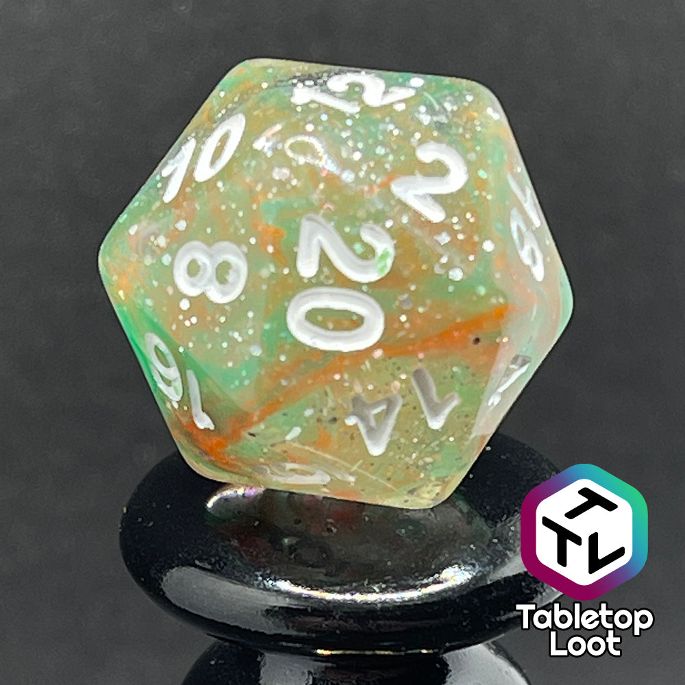 A close up of the D20 from the Star Hatchery 7 piece dice set from Tabletop Loot with swirls of orange and green suspended in glittery clear resin with white numbers.