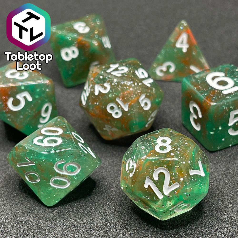 A close up of the Star Hatchery 7 piece dice set from Tabletop Loot with swirls of orange and green suspended in glittery clear resin with white numbers.
