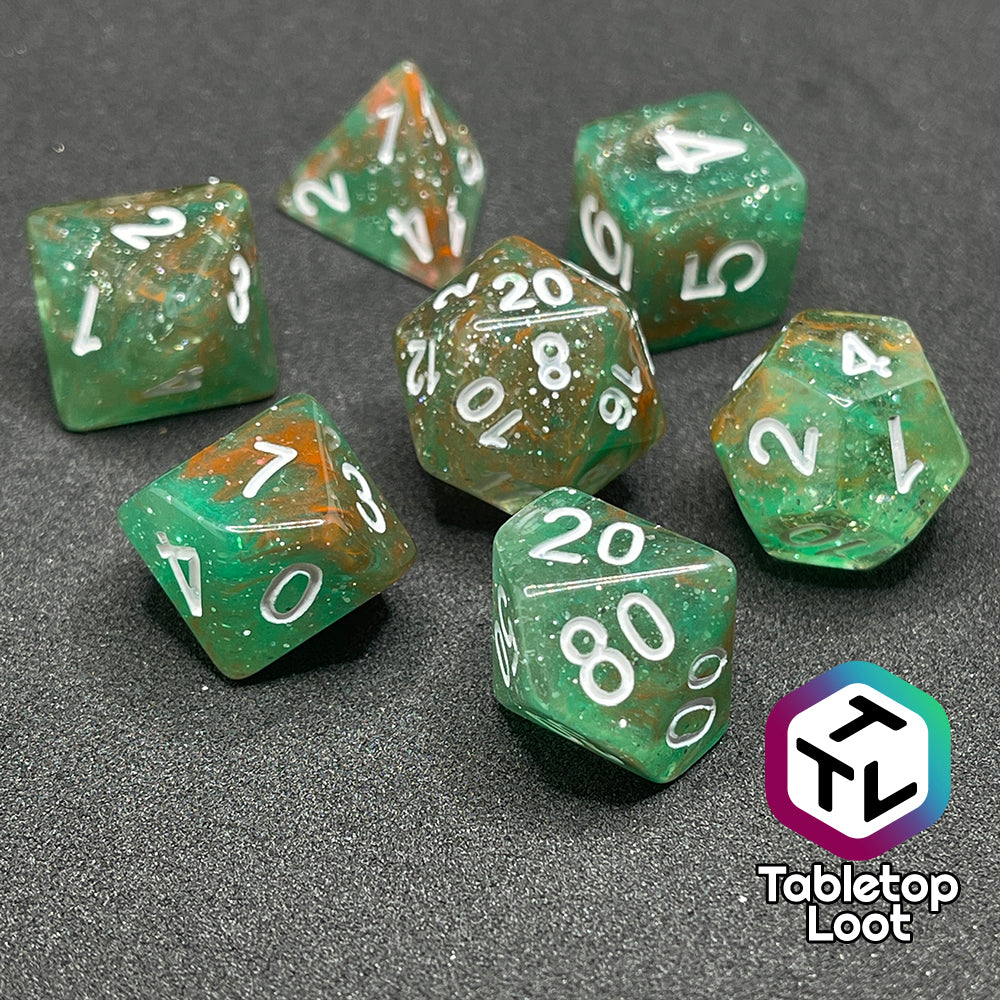 The Star Hatchery 7 piece dice set from Tabletop Loot with swirls of orange and green suspended in glittery clear resin with white numbers.