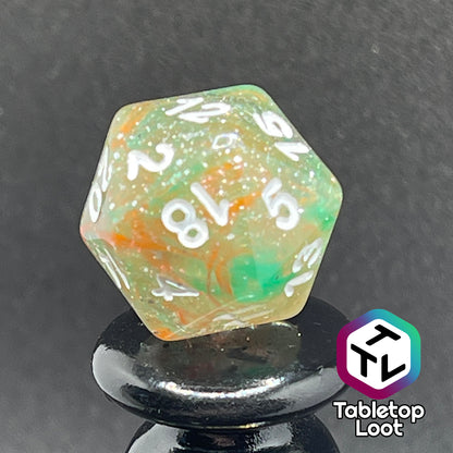A close up of the D20 from the Star Hatchery 7 piece dice set from Tabletop Loot with swirls of orange and green suspended in glittery clear resin with white numbers.