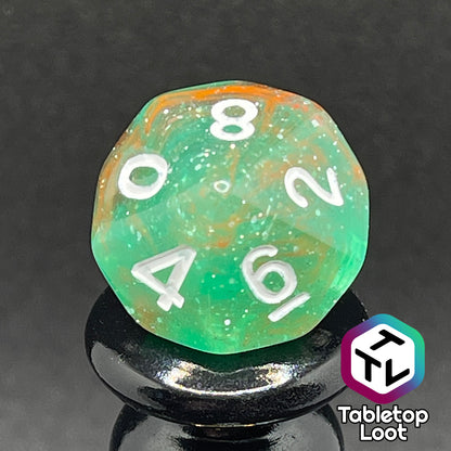 A close up of the D10 from the Star Hatchery 7 piece dice set from Tabletop Loot with swirls of orange and green suspended in glittery clear resin with white numbers.