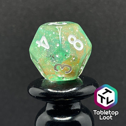 A close up of the D12 from the Star Hatchery 7 piece dice set from Tabletop Loot with swirls of orange and green suspended in glittery clear resin with white numbers.