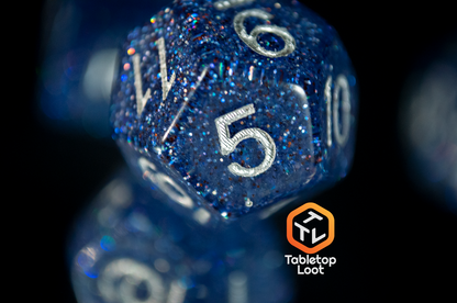 A close up of the D12 from the Starry Form 7 piece dice set from Tabletop Loot packed with blue glitter and silver numbering.