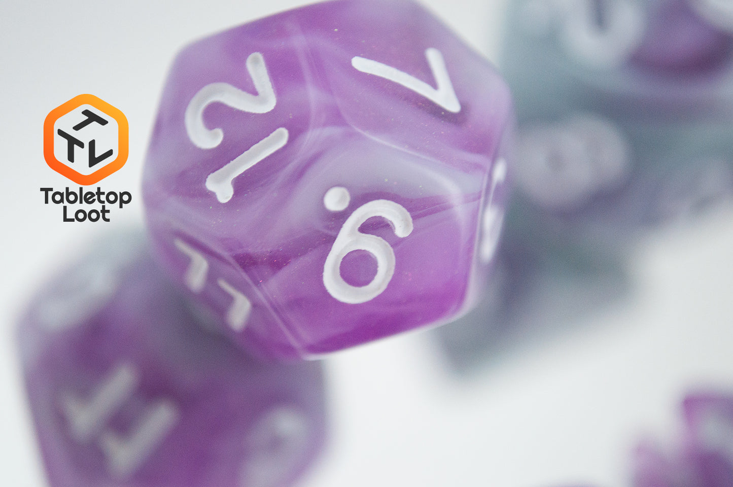 A close up of the D12 from the Stars Shine 7 piece dice set from Tabletop Loot with purple and grey shimmering swirls and white numbering.
