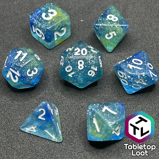 The Stellar Dust 7 piece dice set from Tabletop Loot with wisps of blue and yellow in clear resin and large sparkles with white numbering.