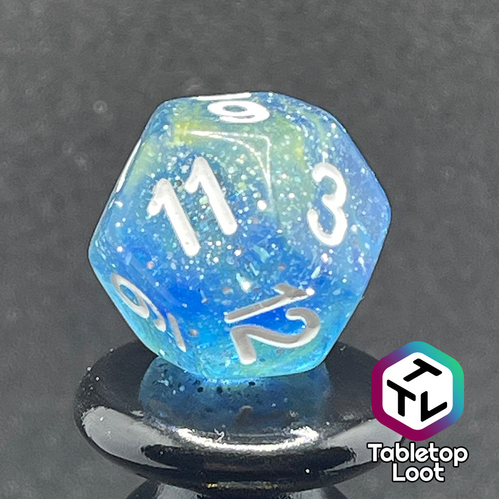 A close up of the D12 from the Stellar Dust 7 piece dice set from Tabletop Loot with wisps of blue and yellow in clear resin and large sparkles with white numbering.