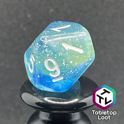 A close up of the D10 from the Stellar Dust 7 piece dice set from Tabletop Loot with wisps of blue and yellow in clear resin and large sparkles with white numbering.