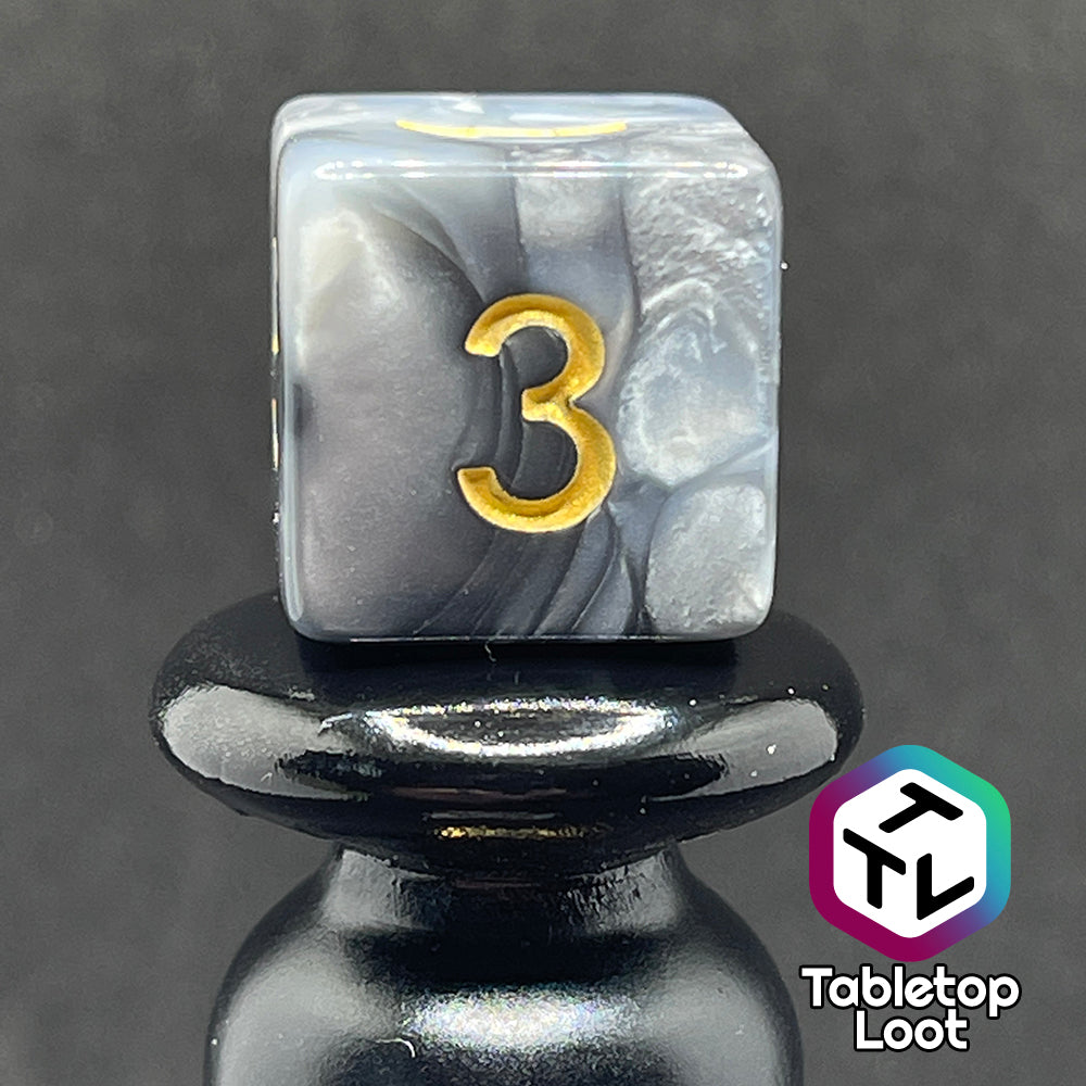 A close up of the D6 from the Stone Giant 7 piece dice set with swirls of iridescent silver and white and gold numbering.