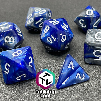 A close up of the Storm Giant 7 piece dice set from Tabletop Loot with swirls of pearlescent blue and silver and white numbering.