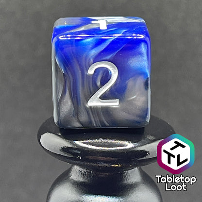 A close up of the D6 from the Storm Giant 7 piece dice set from Tabletop Loot with swirls of pearlescent blue and silver and white numbering.