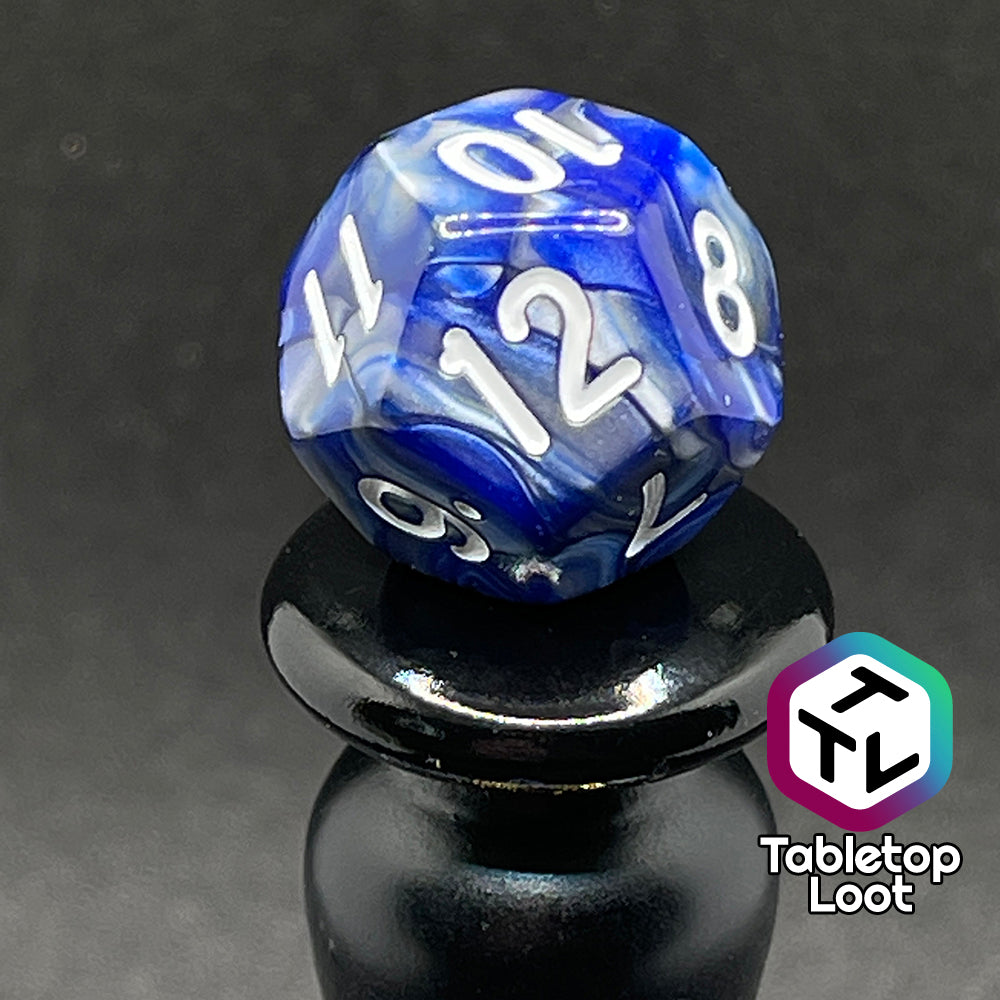 A close up of the D12 from the Storm Giant 7 piece dice set from Tabletop Loot with swirls of pearlescent blue and silver and white numbering.