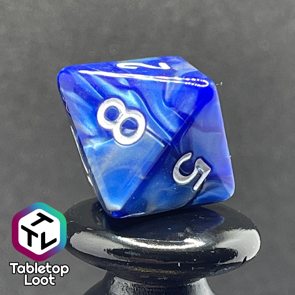 A close up of the D8 from the Storm Giant 7 piece dice set from Tabletop Loot with swirls of pearlescent blue and silver and white numbering.