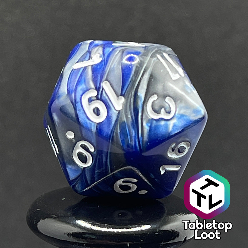 A close up of the D20 from the Storm Giant 7 piece dice set from Tabletop Loot with swirls of pearlescent blue and silver and white numbering.