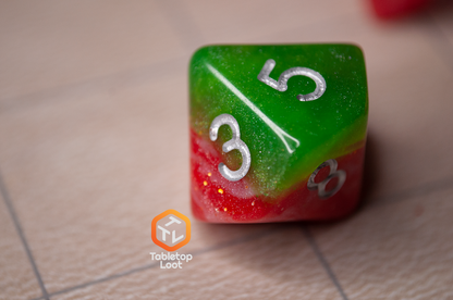 A close up of the D10 from the Strawberry Fields 7 piece dice set with sparkling layers of red and green and silver numbering.