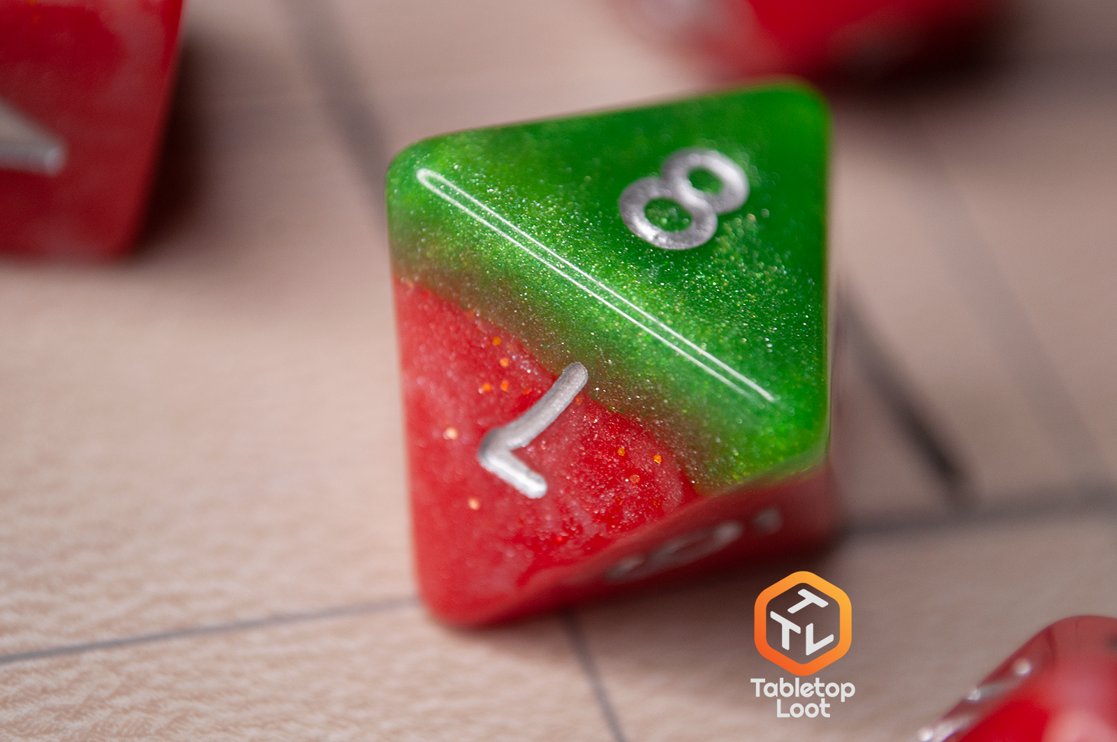 A close up of the D8 from the Strawberry Fields 7 piece dice set with sparkling layers of red and green and silver numbering.