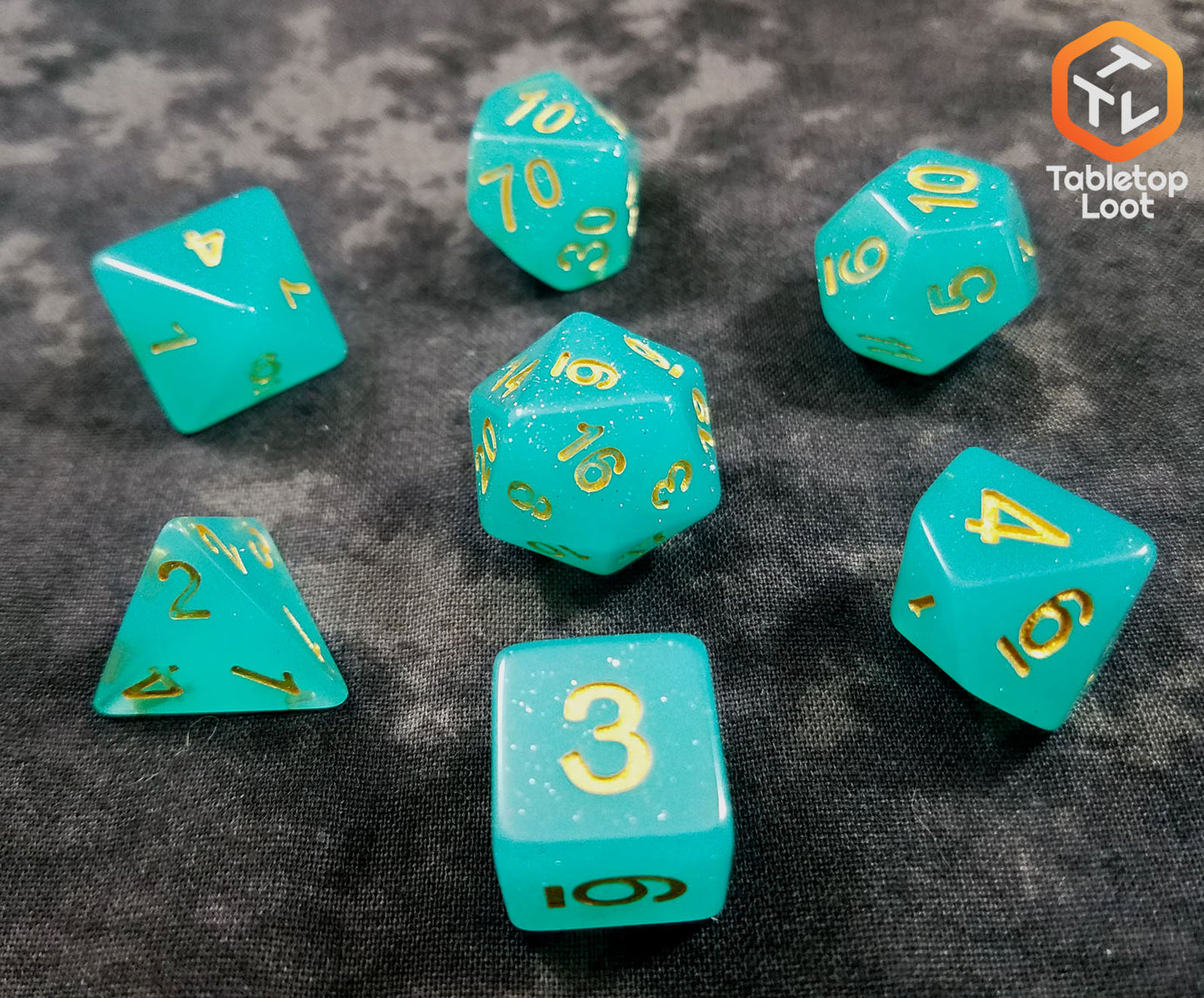 The Blue Beryl 7 piece dice set from Tabletop Loot with a bright glittery aqua resin and gold numbering.